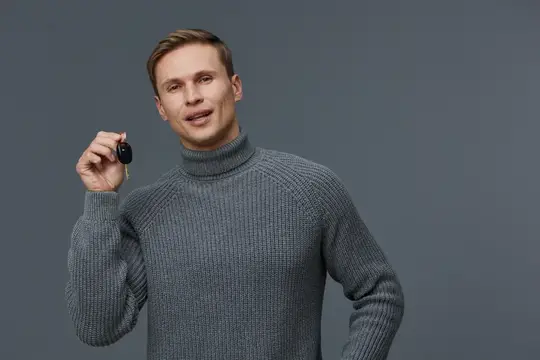 Улыбающийся мужчина в сером свитере держит ключ от машины
