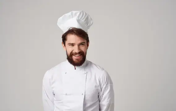 Улыбающийся бородатый повар в белом колпаке на сером фоне
