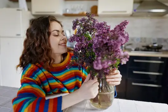 Молодая женщина с закрытыми глазами вдыхает аромат сирени на кухне