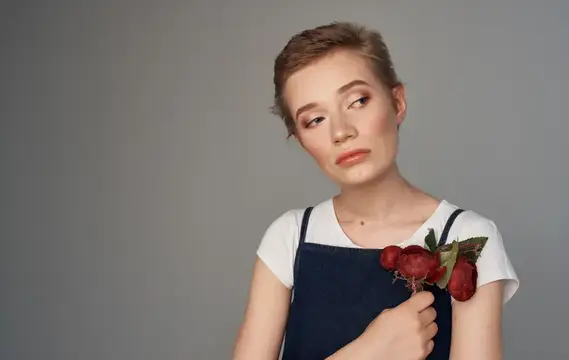 Молодая женщина с веточкой красных ягод у плеча на сером фоне