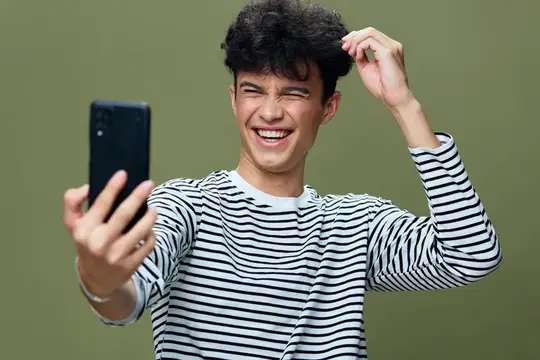 Кудрявый парень в полосатой футболке весело делает селфи