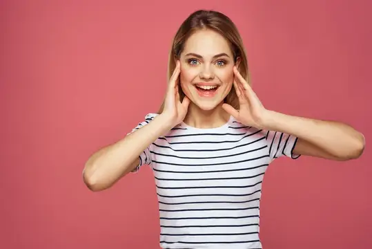Улыбающаяся блондинка в полосатой футболке на розовом фоне