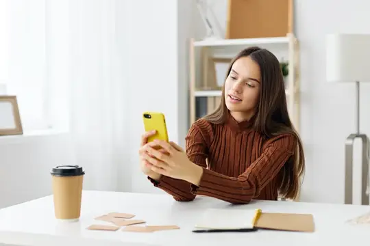 Молодая девушка смотрит в смартфон за белым столом