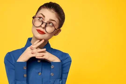 Задумчивая девушка в очках и синей рубашке на жёлтом фоне