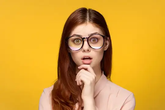 Рыжеволосая девушка в круглых очках удивлённо смотрит на жёлтом фоне