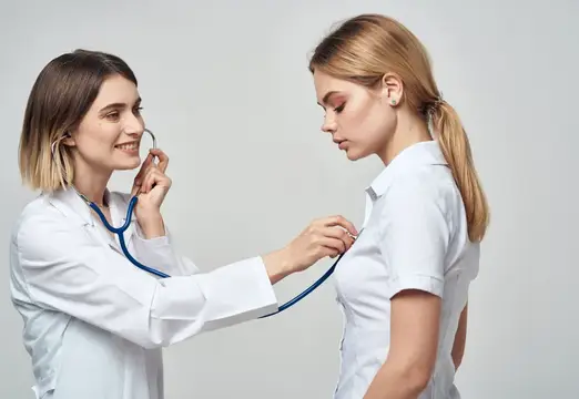 Женщина-врач в белом халате слушает пациентку стетоскопом