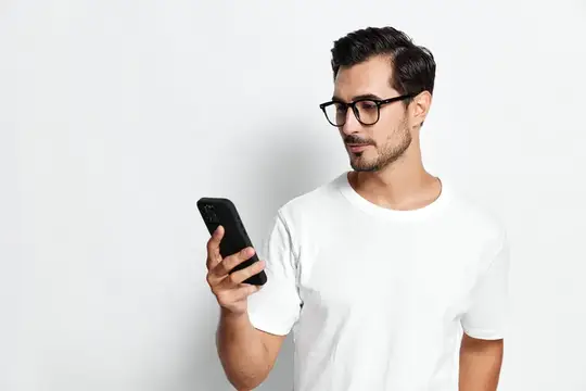 Молодой мужчина в очках смотрит в смартфон на белом фоне