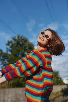 Улыбающаяся девочка в солнечных очках и радужном свитере кружится на улице