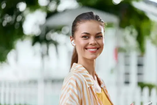 Улыбающаяся девушка в наушниках на фоне зелени