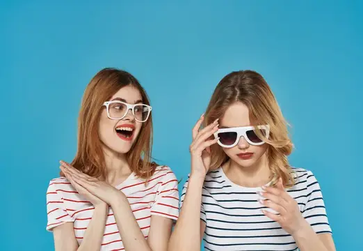 Две смешливые девушки в белых очках на голубом фоне