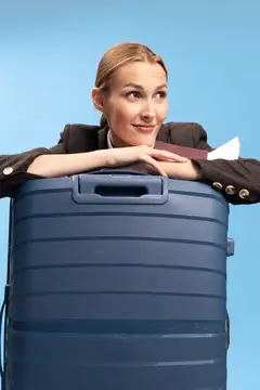 Улыбающаяся светловолосая женщина облокотилась на большой синий чемодан