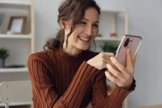 Улыбающаяся темноволосая женщина смотрит в смартфон дома
