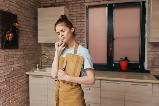 Задумчивая молодая женщина в фартуке с ножом на кухне