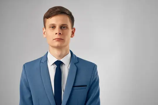Молодой человек в синем костюме и галстуке на сером фоне