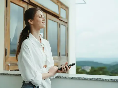 Молодая женщина со смартфоном отдыхает на балконе с видом на горы