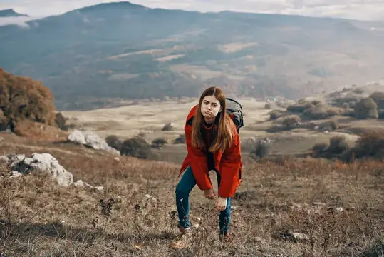 Уставшая девушка с рюкзаком отдыхает на горном склоне