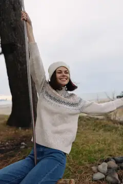 Улыбающаяся девушка в свитере качается на качелях у дерева