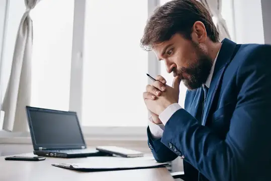 Бородатый мужчина сидит за столом перед ноутбуком, изучая финансовые технологии