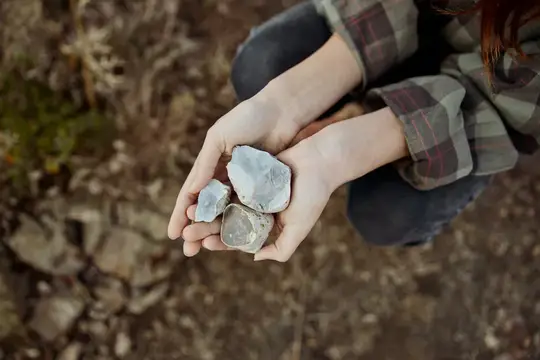 Руки девушки держат куски светлого камня на фоне земли
