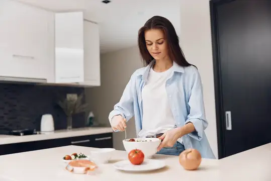 Молодая женщина готовит салат на светлой кухне