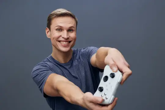 Улыбающийся парень протягивает белый игровой контроллер на сером фоне