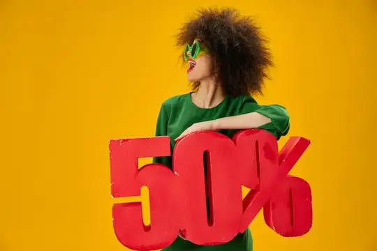 Кудрявая девушка в зелёном платье держит красную скидку 50% на жёлтом фоне