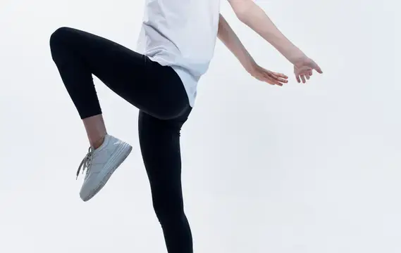 Спортивная девушка в чёрных леггинсах высоко поднимает колено