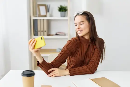 Улыбающаяся девушка с жёлтым смартфоном за столом в офисе