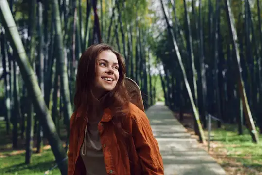 Улыбающаяся девушка с рюкзаком гуляет по бамбуковой роще