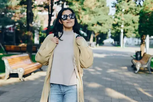 Улыбающаяся азиатская девушка в солнечных очках гуляет по парку