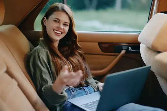 Улыбающаяся девушка с ноутбуком на заднем сиденье автомобиля