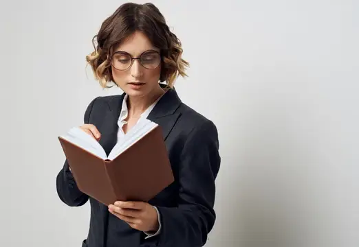 Молодая женщина в очках и деловом костюме читает книгу