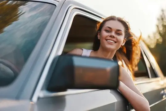 Улыбающаяся девушка высунулась из окна автомобиля на закате