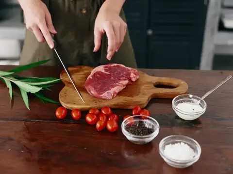 Повар нарезает кусок сырого мяса на деревянной доске