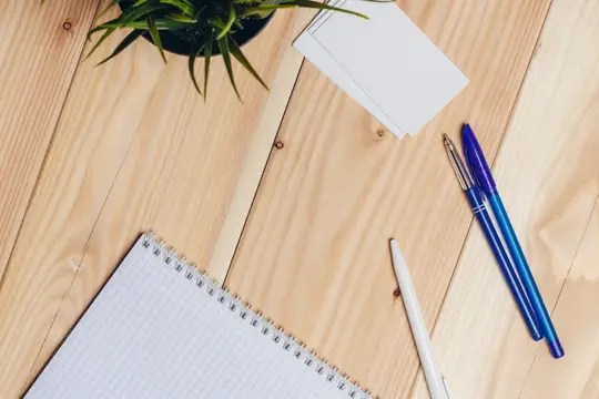 Блокнот, ручки и растение на светлых деревянных досках