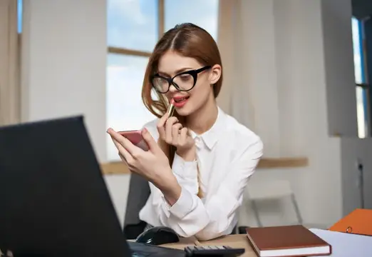 Молодая женщина в очках смотрит в смартфон в офисе