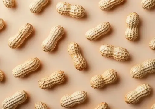 Плоская композиция из сырого арахиса в скорлупе, равномерно рассыпанного на нейтральной бежевой поверхности
