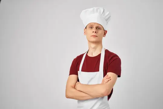 Молодой повар в колпаке и фартуке со скрещёнными руками