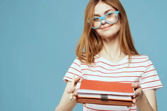 Рыжеволосая девушка в очках с стопкой книг на синем фоне