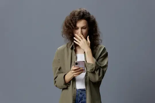 Кудрявая женщина с телефоном удивлённо прикрывает рот рукой