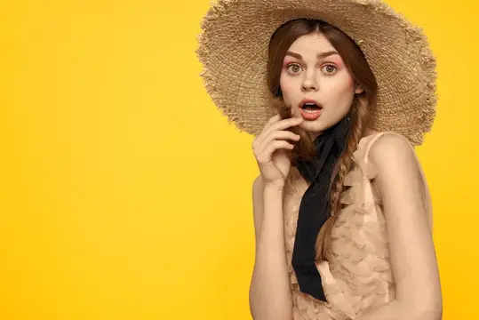 Удивлённая девушка в соломенной шляпе на жёлтом фоне