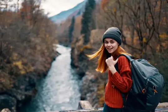 Весёлая женщина-туристка в осеннем лесу, горы и река