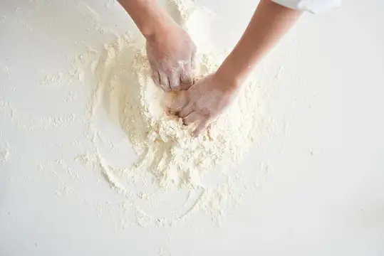 Руки замешивают тесто в муке на белом столе