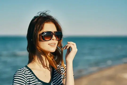 Красивая женщина-модель в солнцезащитных очках стоит у моря в горах