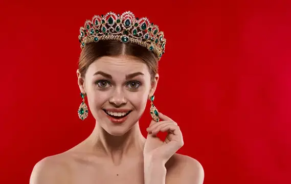Улыбающаяся девушка в короне с изумрудами на красном фоне