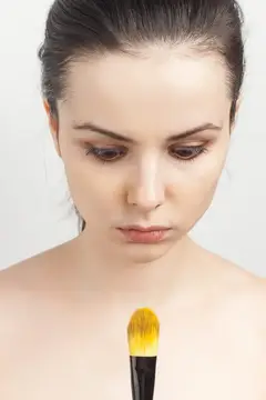Молодая женщина с кистью для макияжа смотрит вниз на белом фоне