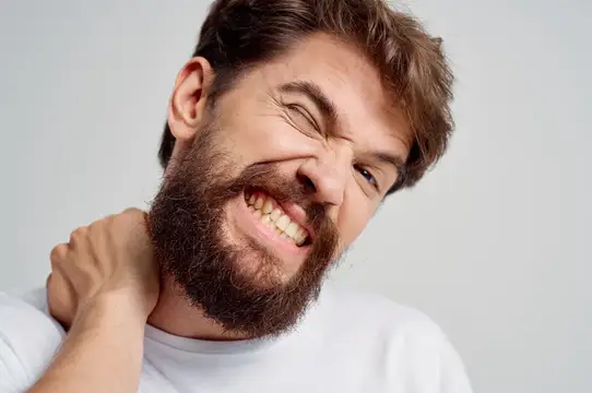 Бородатый мужчина с гримасой боли держится за шею