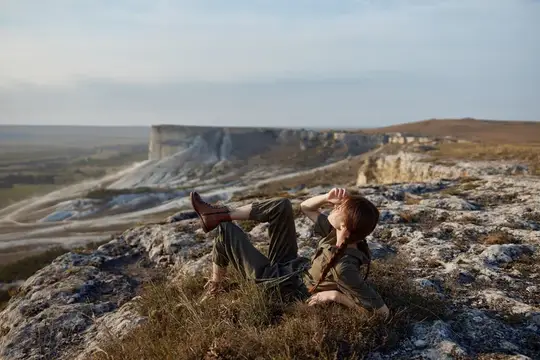 Молодая женщина отдыхает на скалистом склоне над долиной