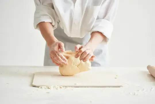 Женщина в белом фартуке замешивает тесто на светлой кухне