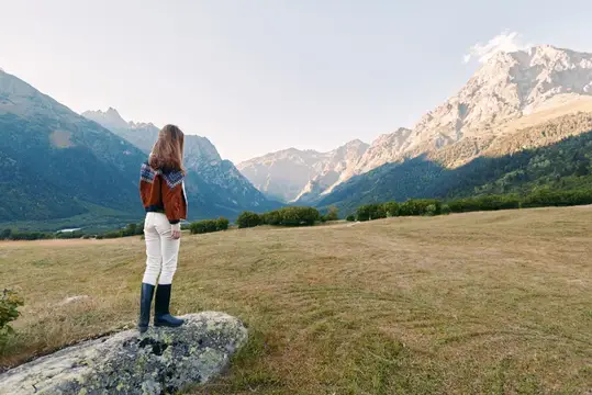 Девушка стоит на камне и смотрит на горную долину